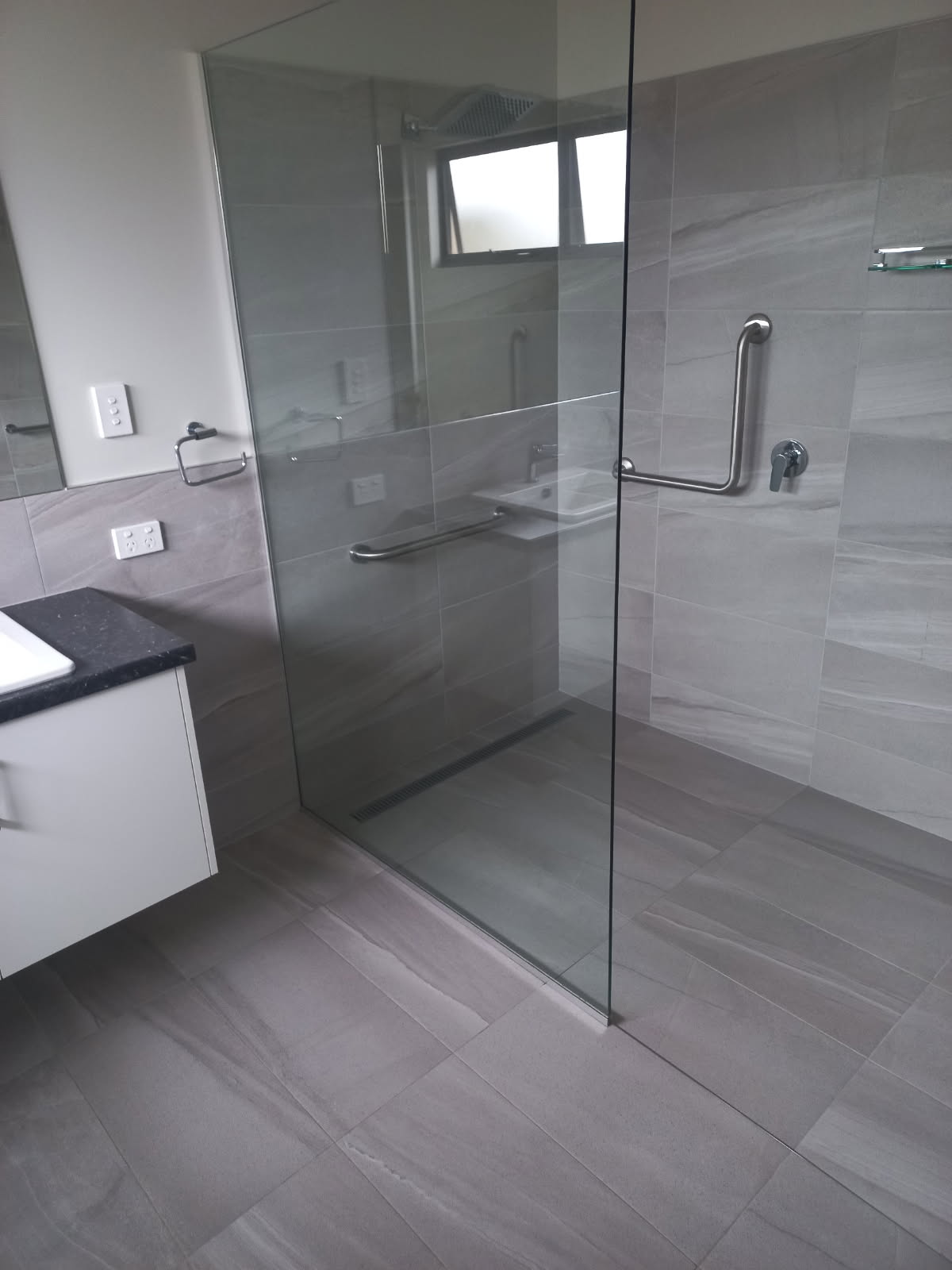 A grey tiled bathroom and walk in shower after a tile and grout clean
