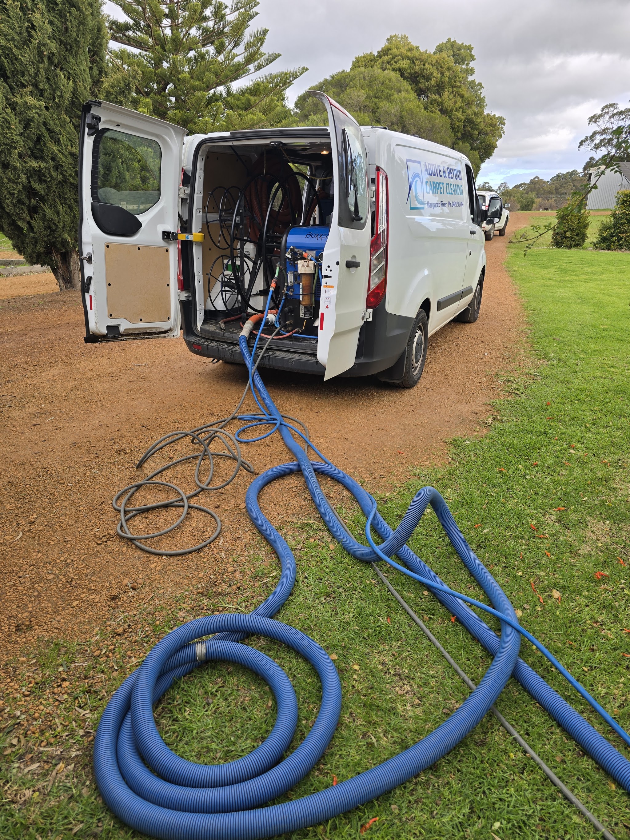 The van backed onto a rural driveway with the extraction unit inside and hoses run out across the lawn